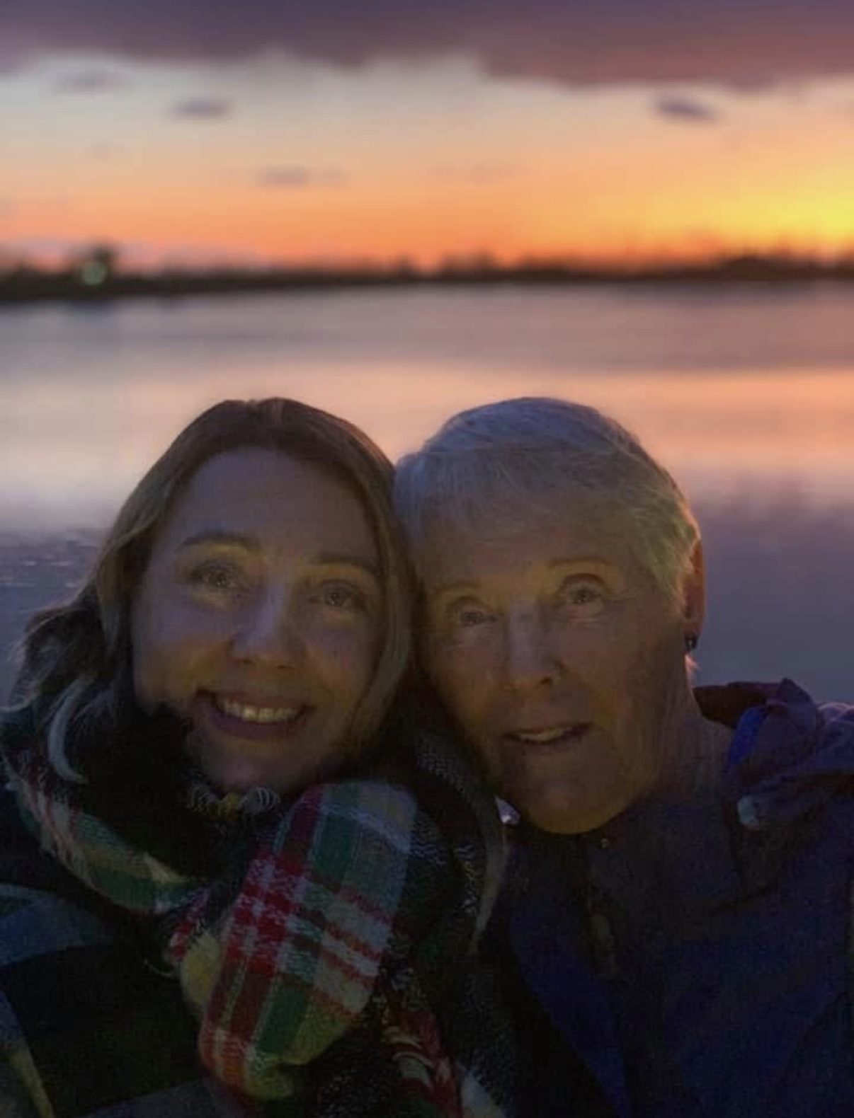 Laura and a loved one in a selfie at a lakeside sunset