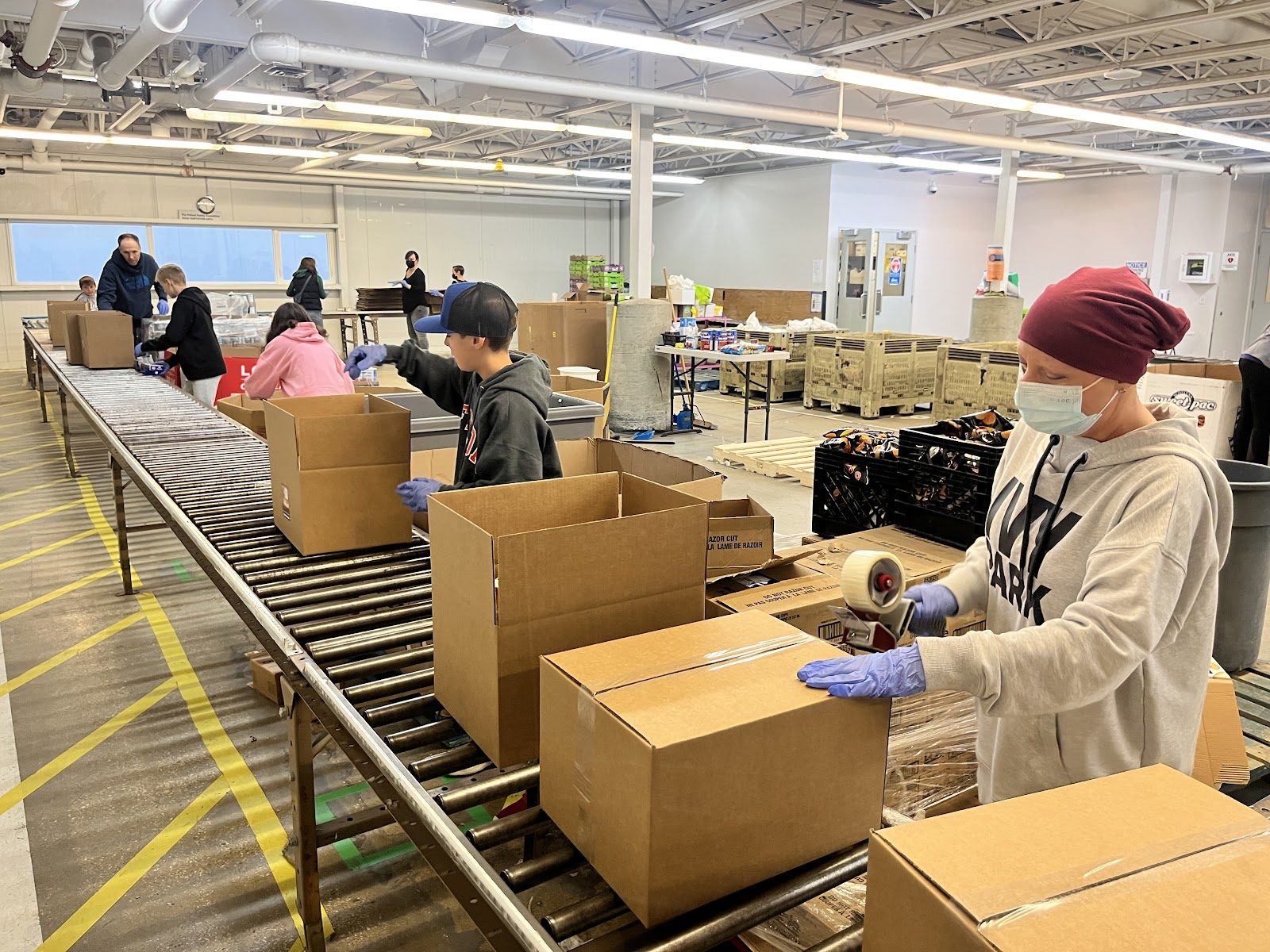Volunteers packing cardboard boxes along a conveyor line