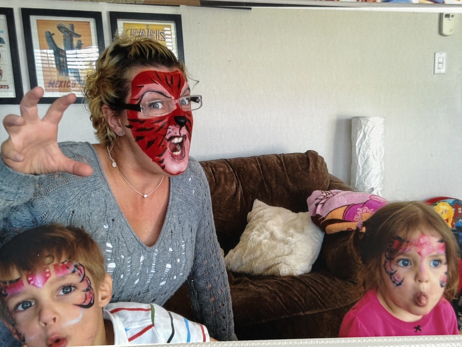 Laura in red face paint pulling a silly face with two face-painted children