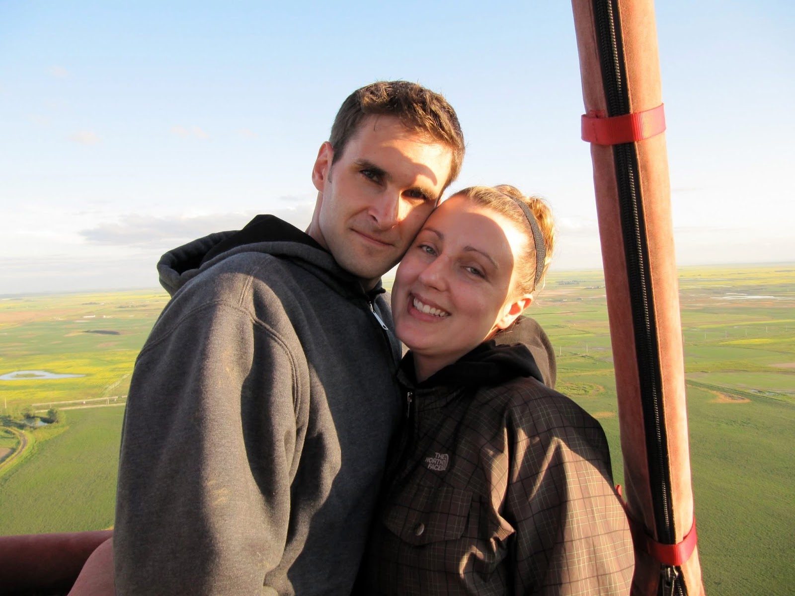 Laura and Chad together in a hot-air balloon above green fields