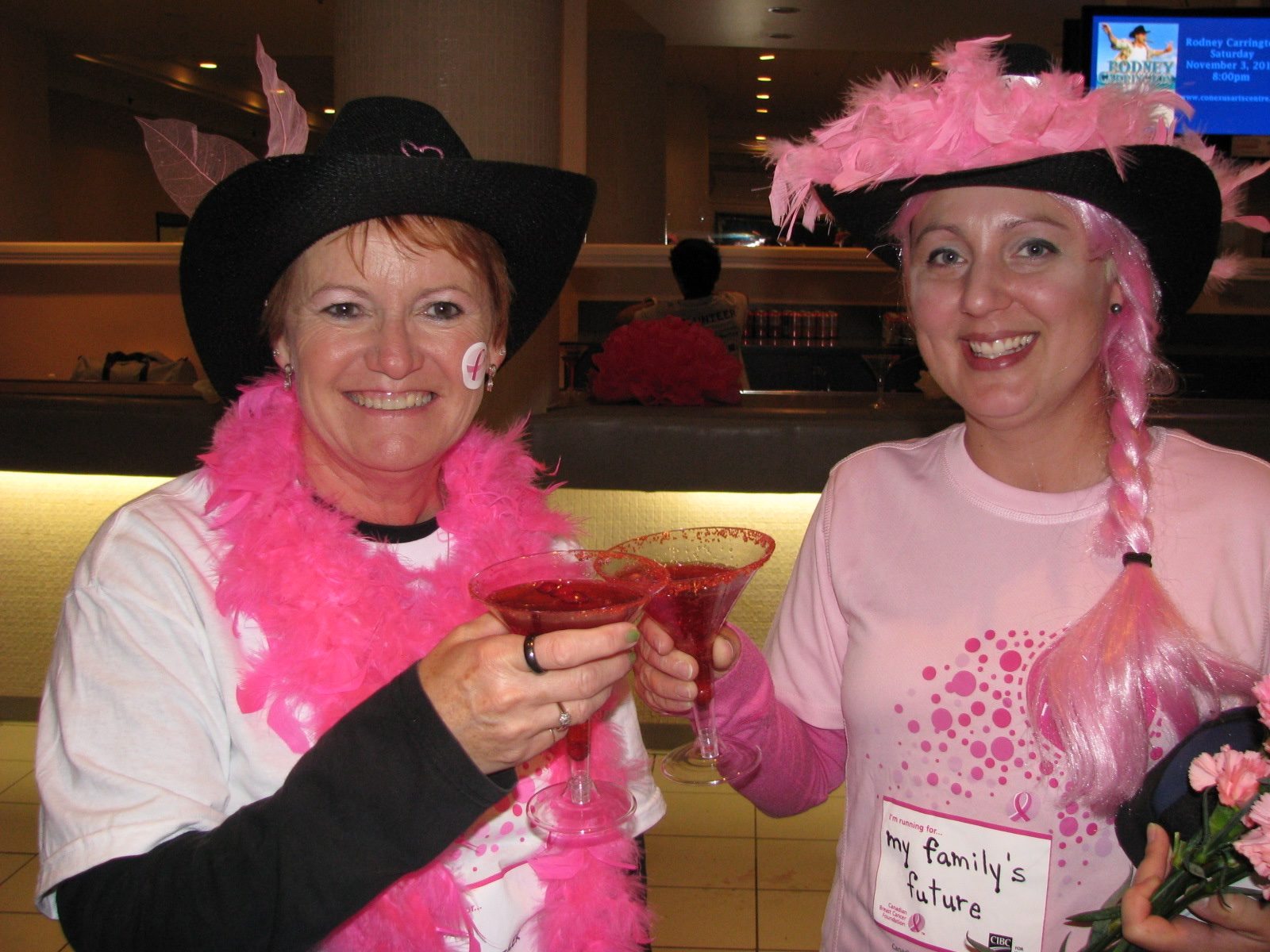 Laura and a friend toasting in pink cowboy hats and feather boas