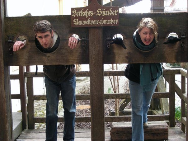 Laura and Chad laughing with their heads in old wooden stocks while travelling